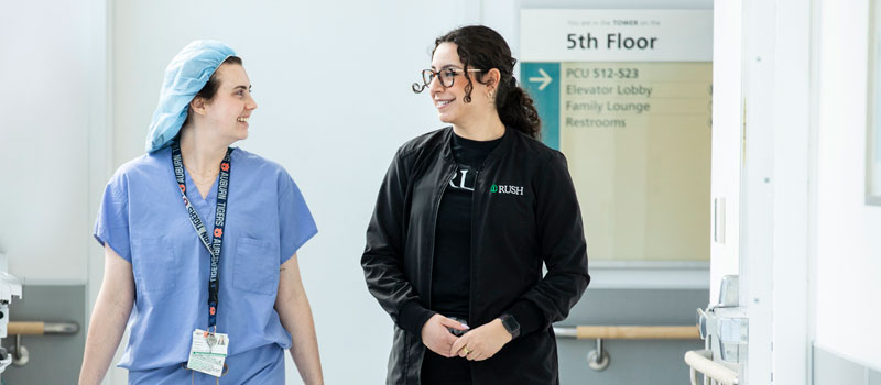 Two Rush nurses walk through a Rush University Medical Center hallway while talking to each other