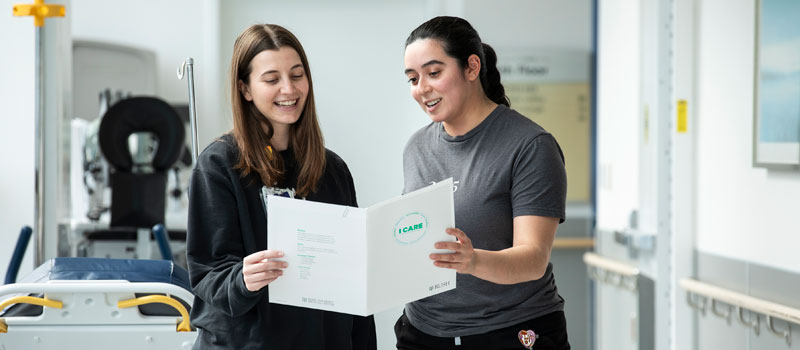 Two Rush nurses hold a patient handoff document and discuss the instructions within
