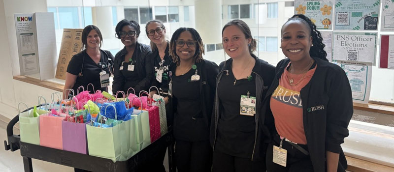 Six Rush nurses stand behind a table with colorful care bags for women at SisterHouse Recovery Home