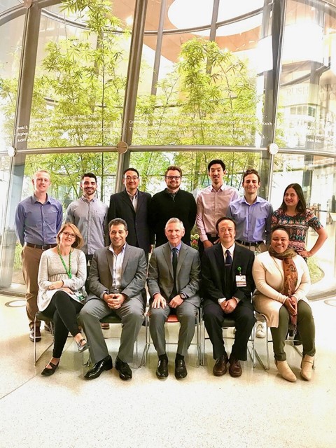 Dr. Fessler, front and center, seated with a group of students in a bright atrium with floor-to-ceiling windows.
