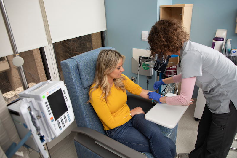 A nurse checks something on the arm of a patient, who is seated.
