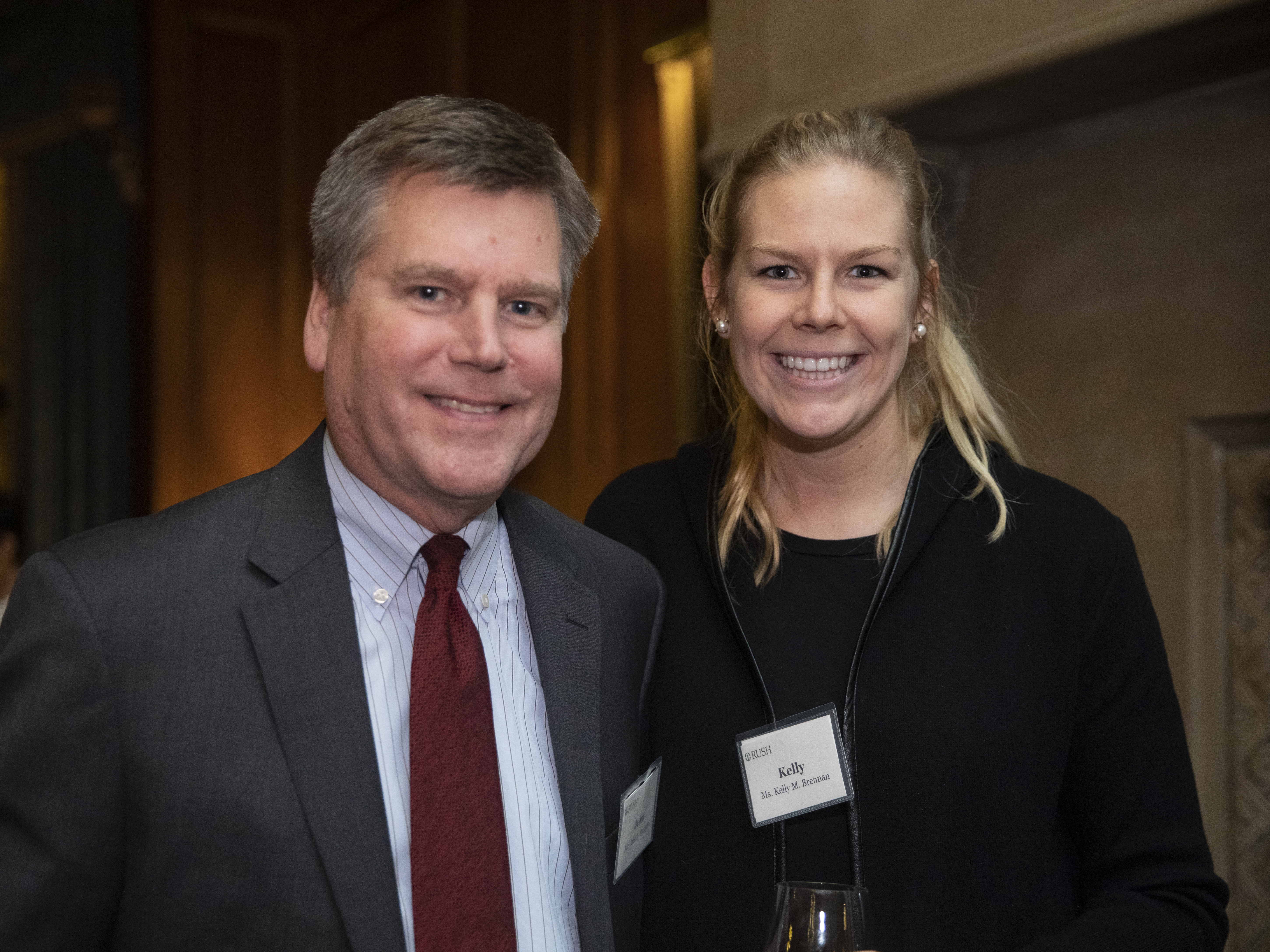 Two people standing together at an indoor event, wearing name tags.
