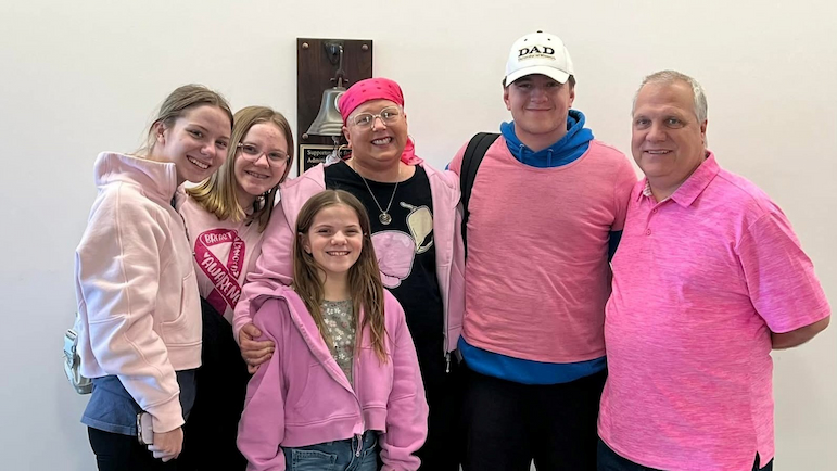 Julie Lechet stands with a group of people, all wearing pink, near the survivor's bell at Rush.