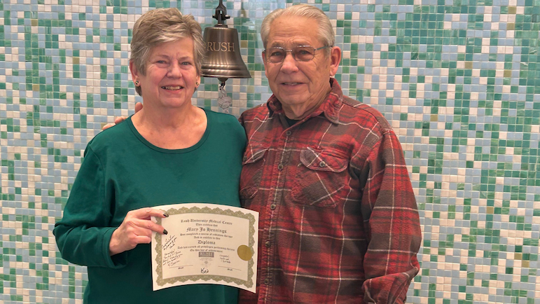 Mary J. Hennings holds up a certificate while standing alongside someone at the survivor's bell at Rush.