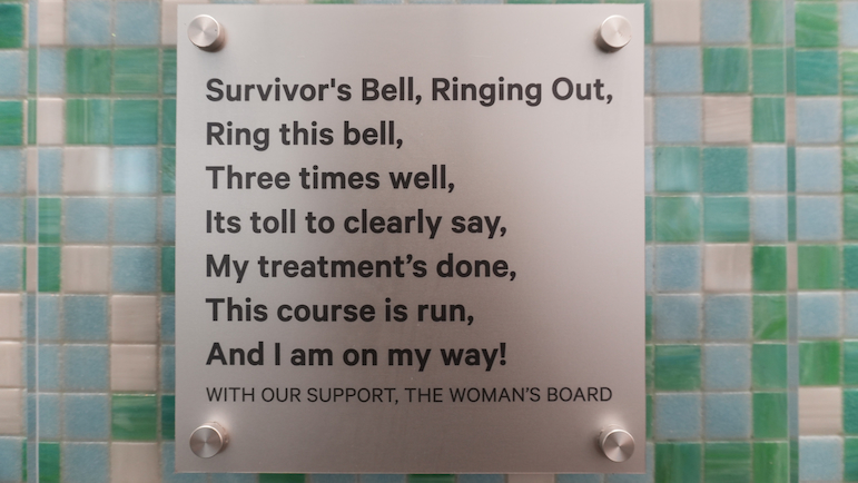 A place on a tiled wall reads: Survivor's Bell, Ringing Out, Ring this bell, Three times well, Its toll to clearly say, My treatment's done, This course is run, And I am on my way! (With Our Support, The Woman's Board)