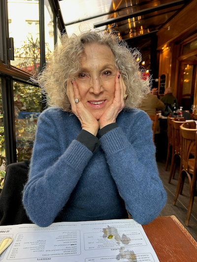 Sherry Koppel, in a blue sweater, smiles with her head resting in her hands