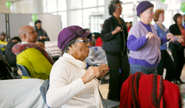 A group exercise program, with a seated woman wearing a purple hat in focus in focus