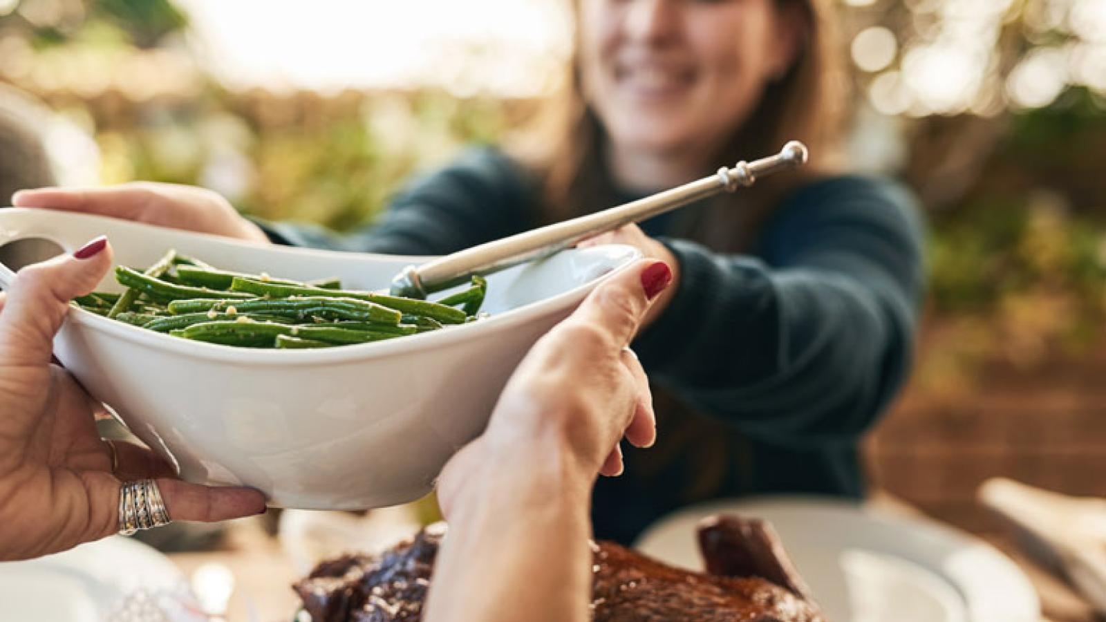 One Woman Passing a Bowl of Green Beans to Another Woman Across the Holiday Table