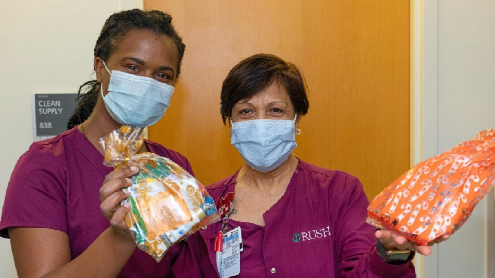 Two health care workers in scrubs and masks hold up colorful care packages