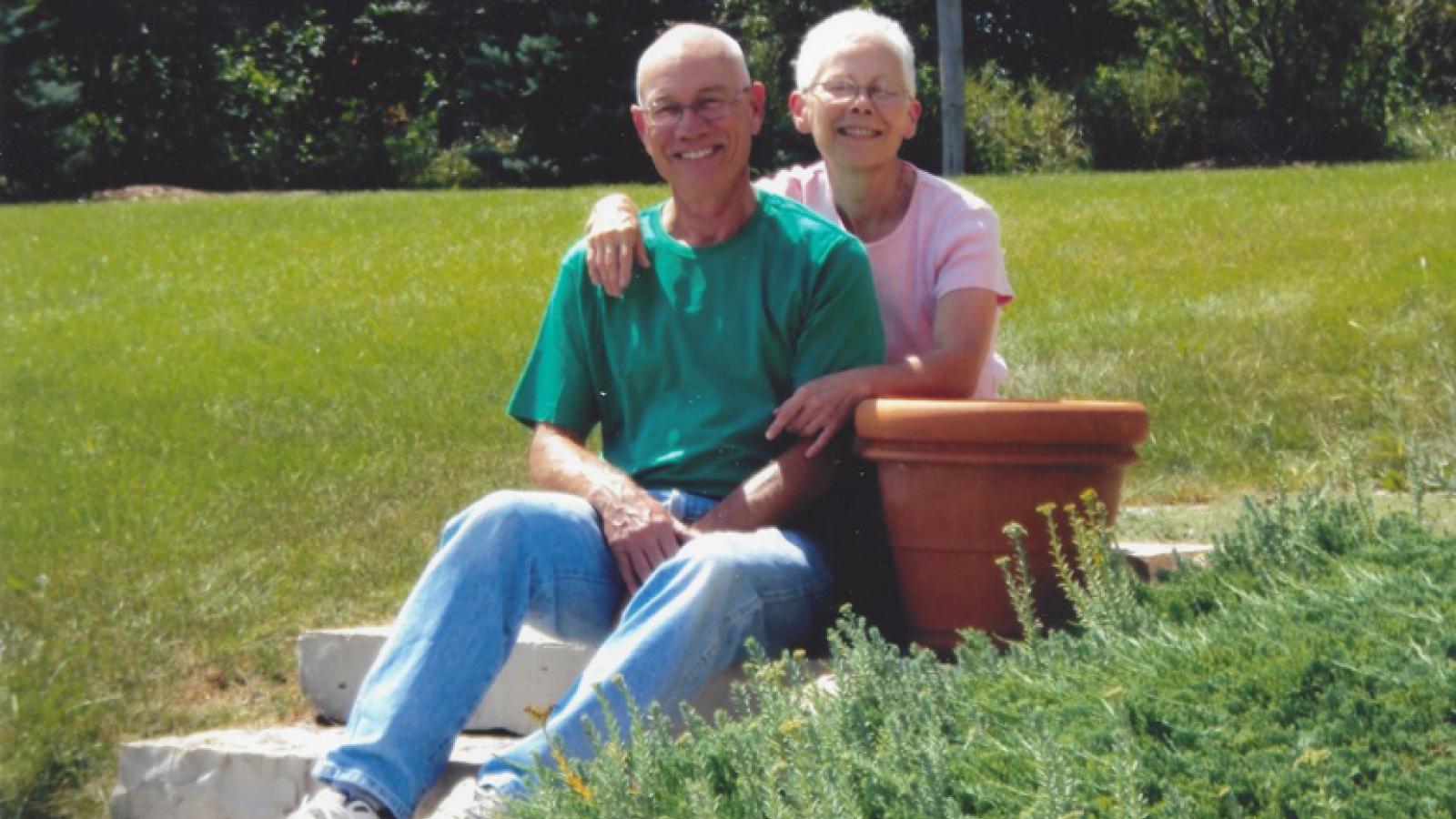 Mark, in green, and Anne, in pink sit in a grassy yard.