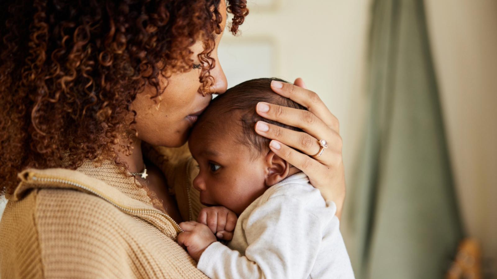 A mother holding a baby on her chest and kissing the baby's head.