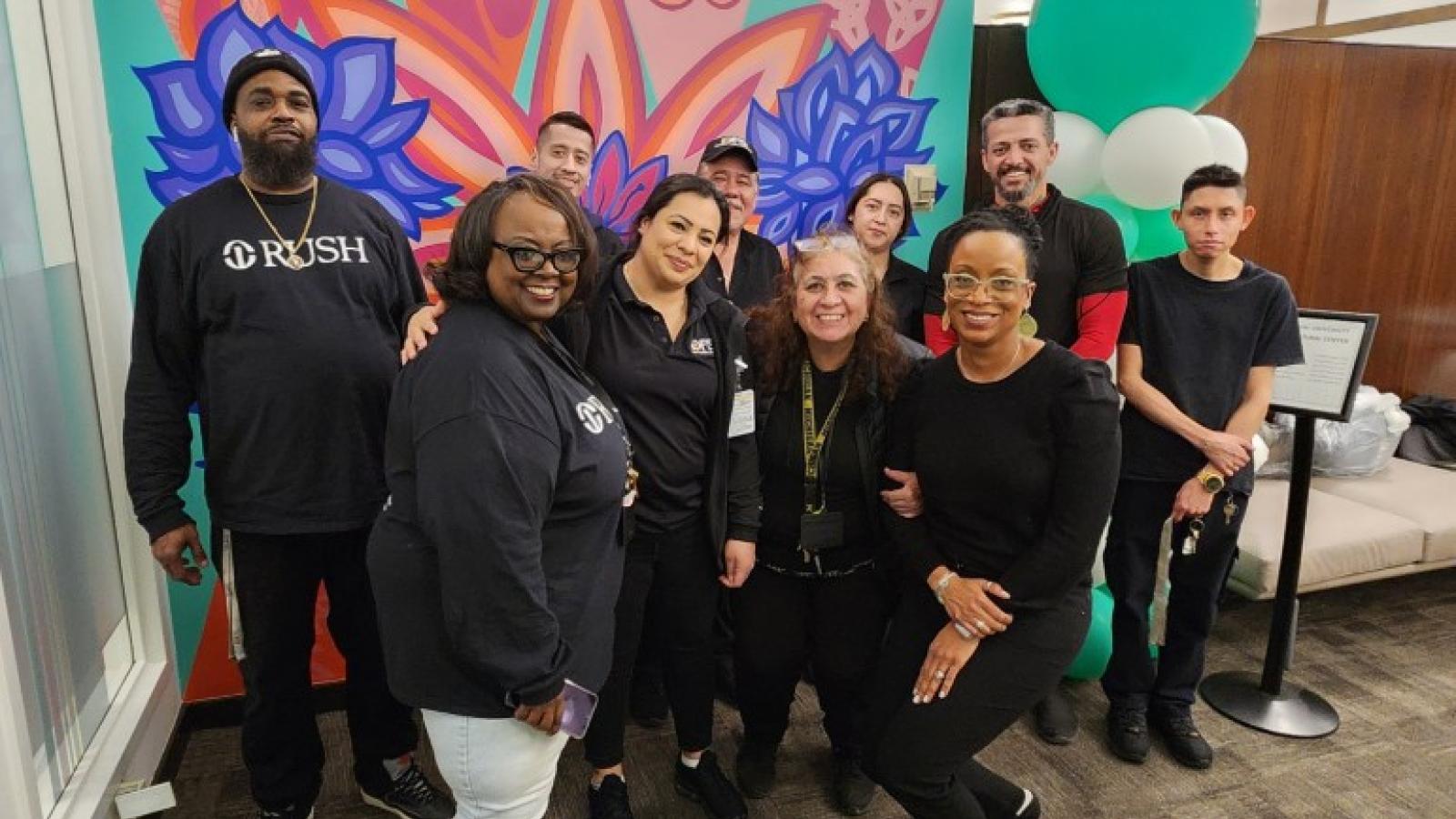 Rush faculty smile in front of a mural in the Cultural Center