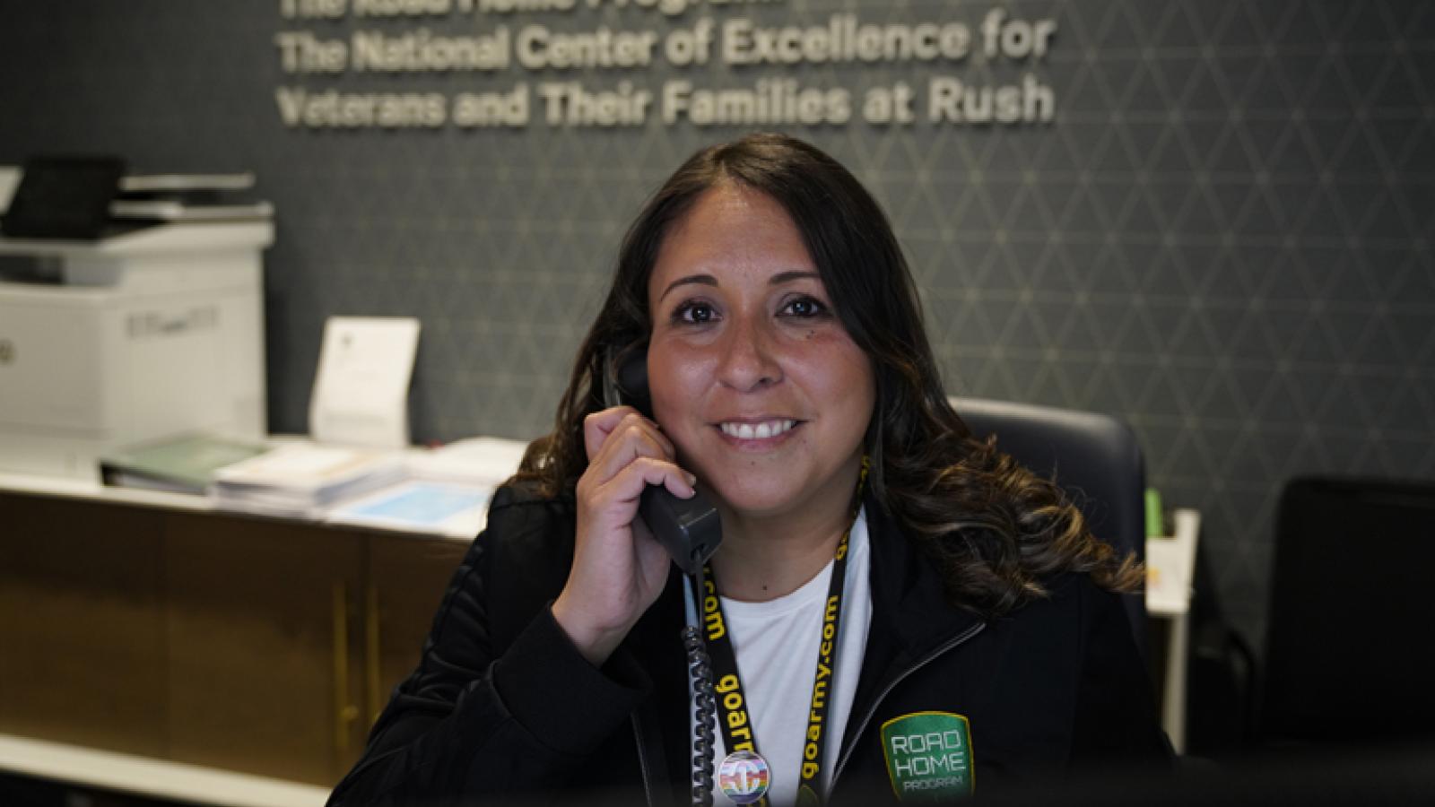 Dee Garcia, a woman with long brown hair and a smile on her face, talks on the phone while working at the Road Home Program.