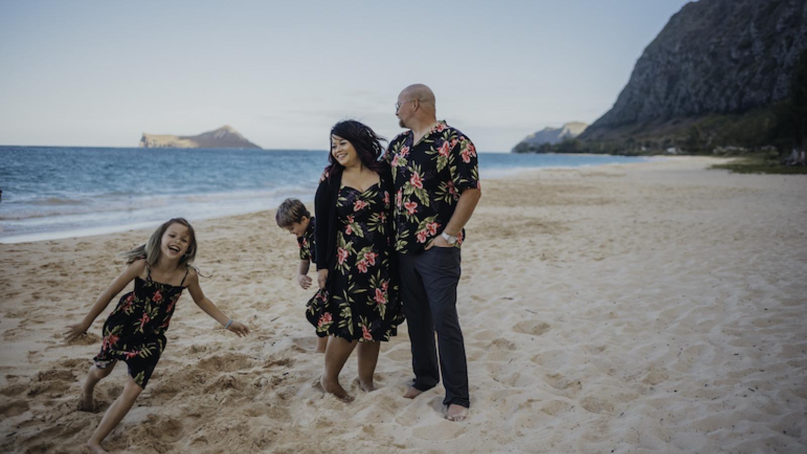 Fitha Dahana-Ellis stands on the beach with her husband and two children, who are running in the sand.