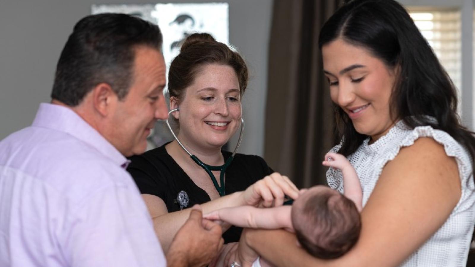 A mother and father hold a baby while a nurse uses a stethoscope to listen to the baby's heart