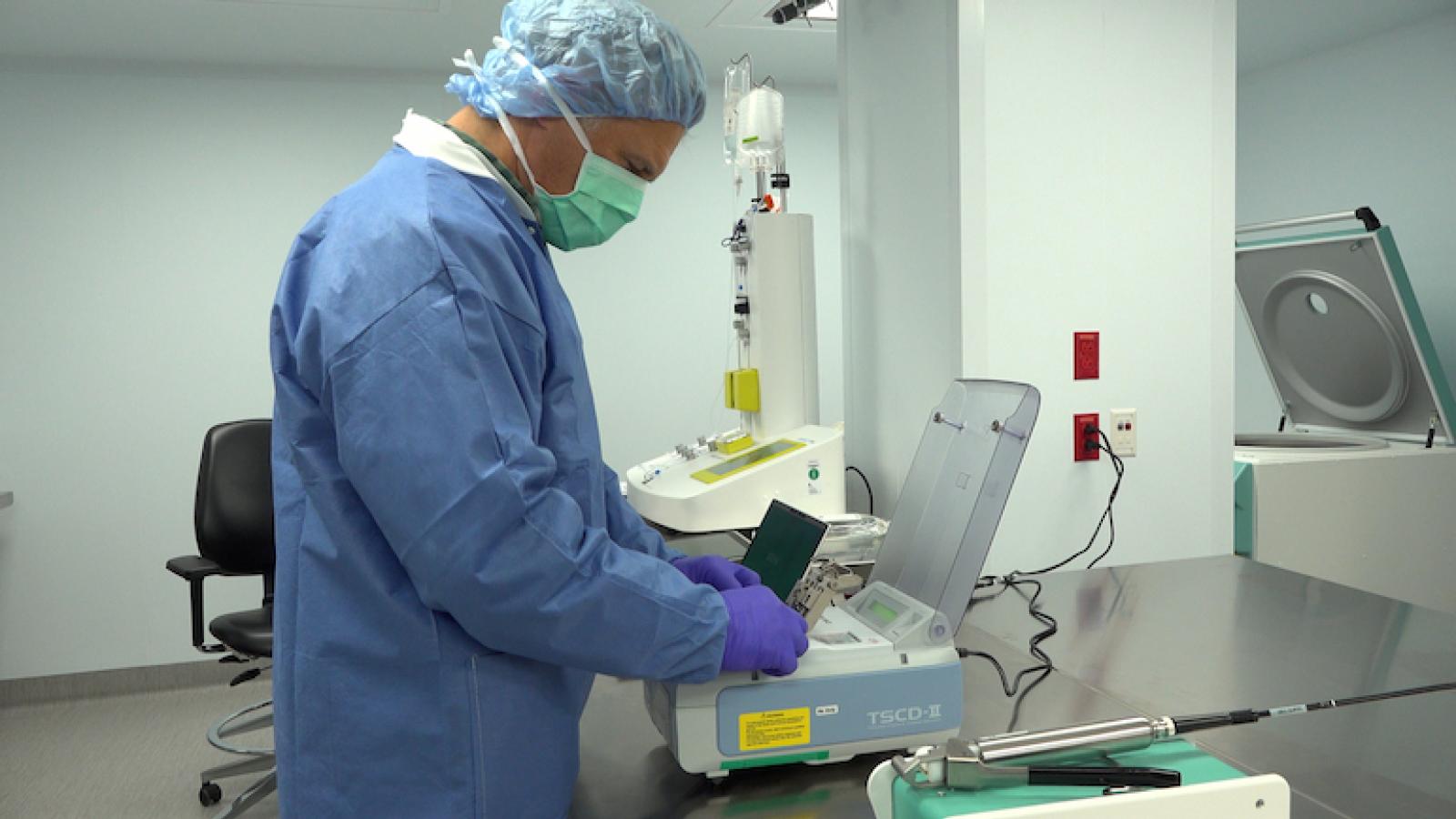 Someone in a gown and mask stands at a machine.