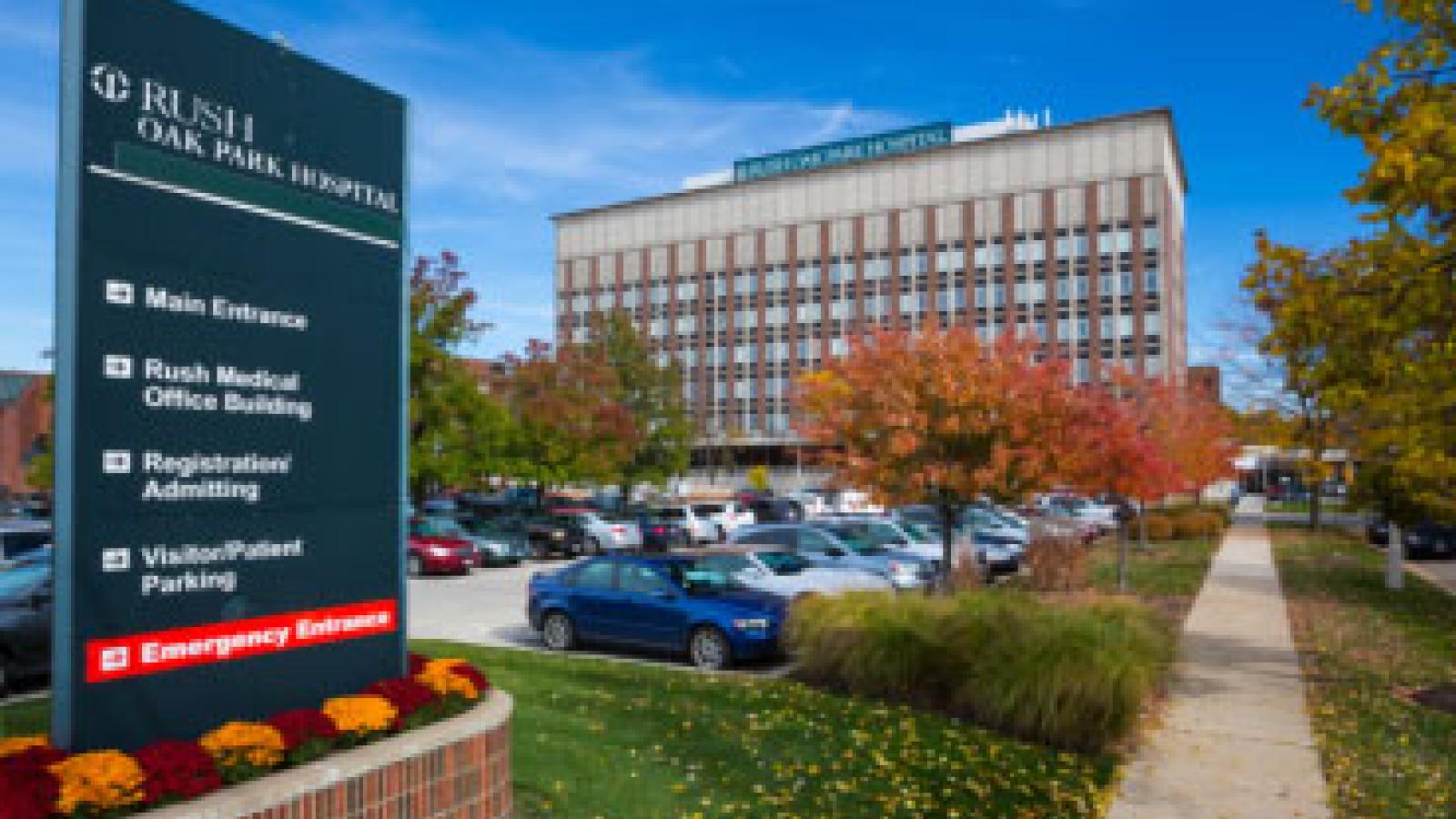 Front view of RUSH Oak Park Hospital on a sunny day with blue skies. A sign in the foreground directs patients and visitors where to go for various services.