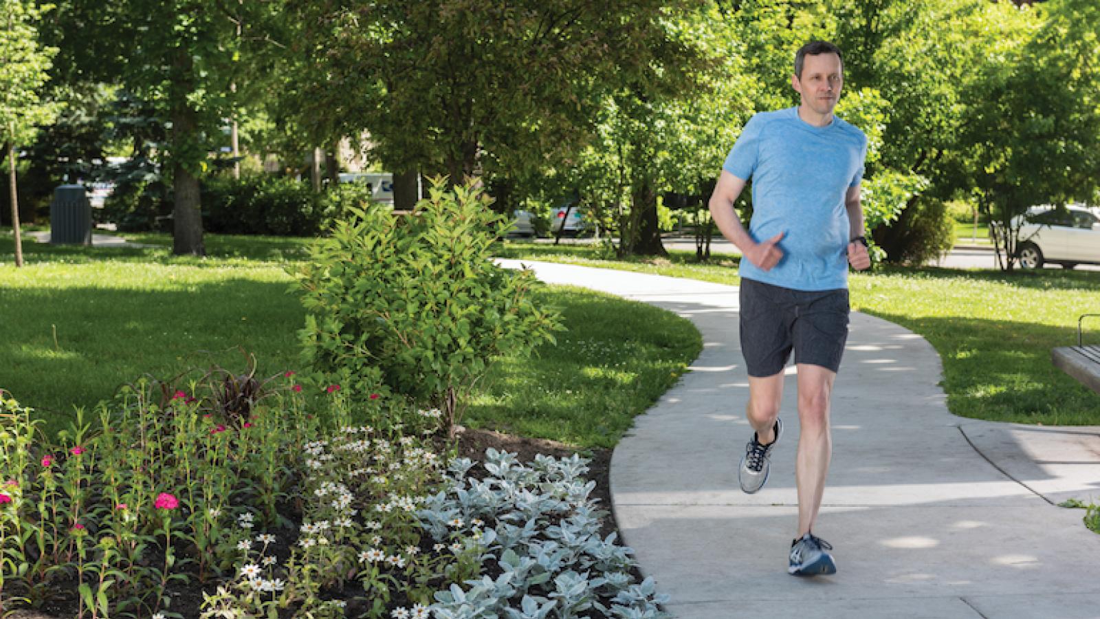 A man runs down a path, with greens and flowers blooming around the path.