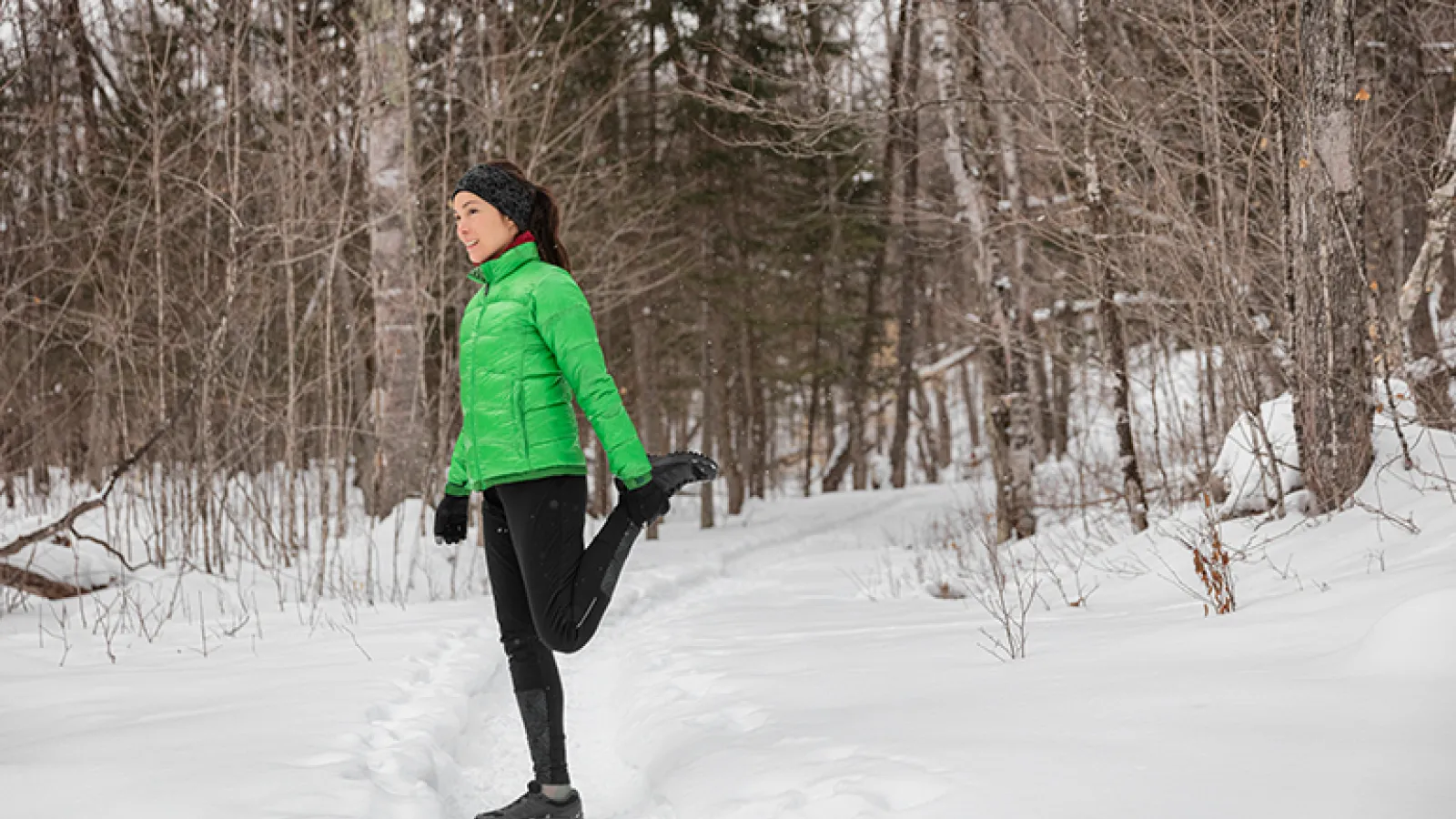 A woman in a green jacket stretching in the snow
