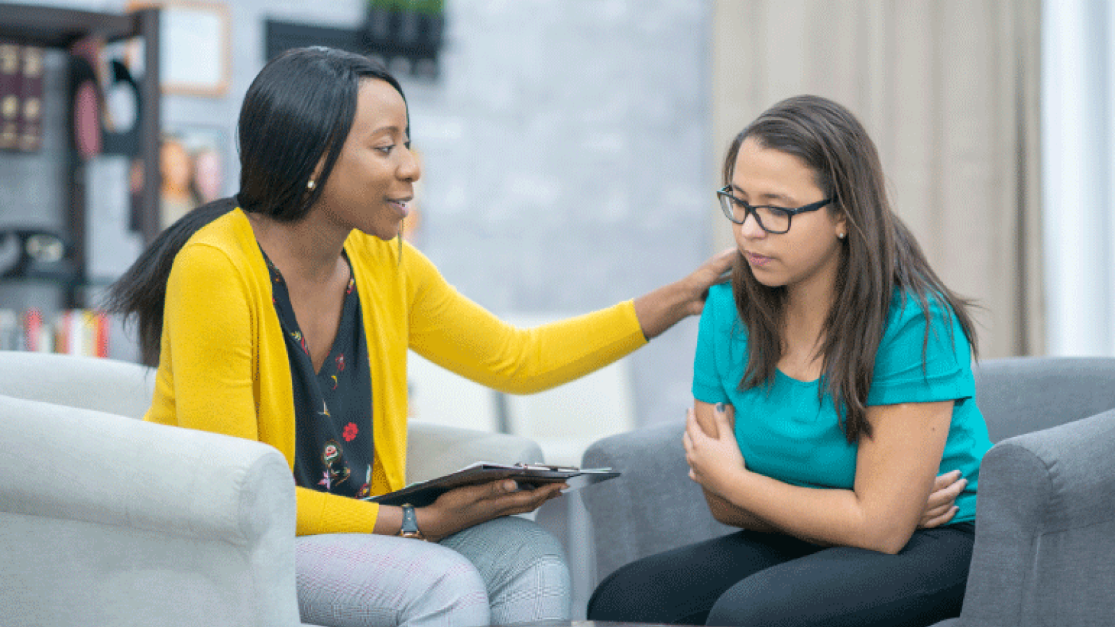 Black female care provider with hand on shoulder of female patient of color