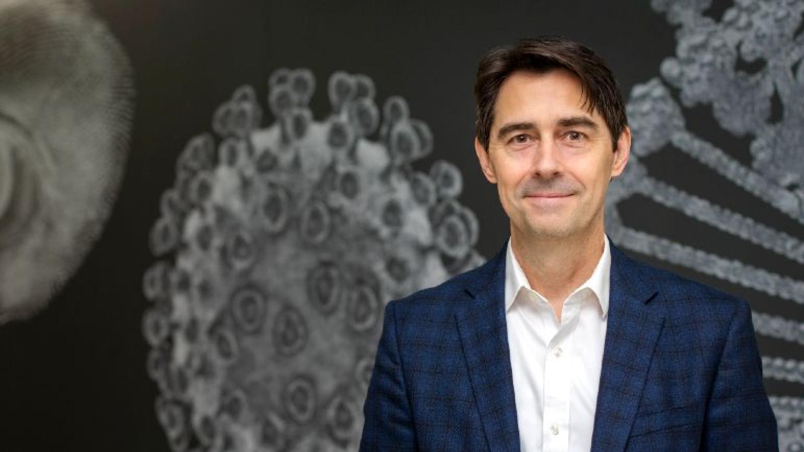 A man wearing a suit in front of a background of microscopic images