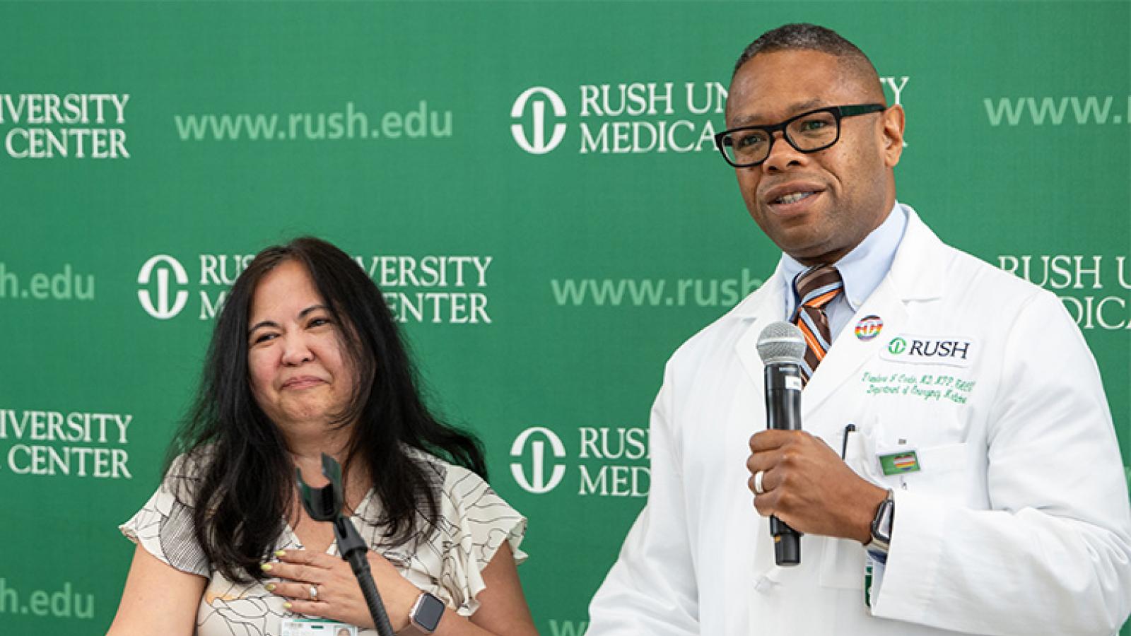 anna candoleza muglia with her hand over her heart as ted corbin talks into a microphone