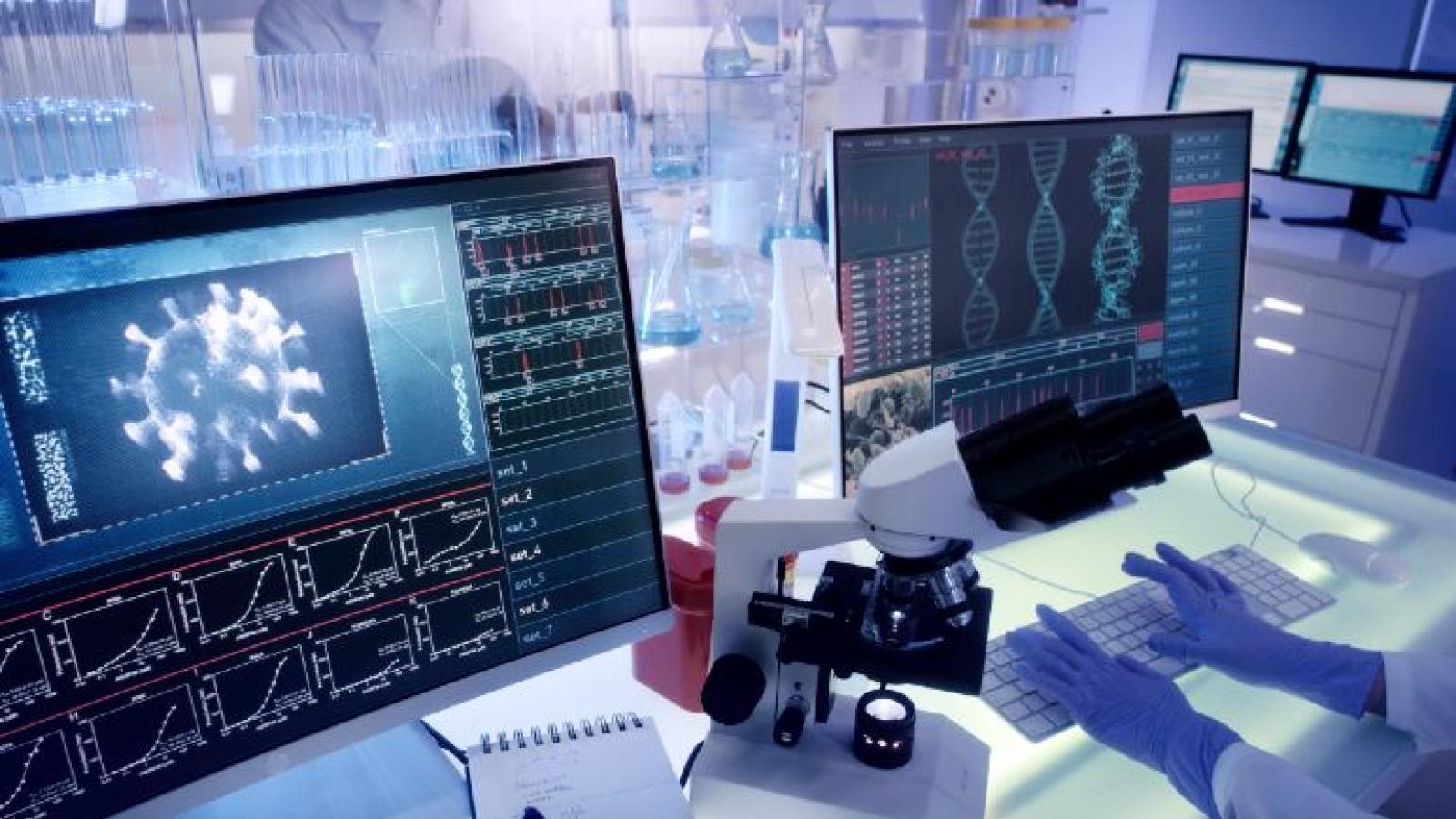 Gloved hands using a computer for imaging with lab glassware in the background