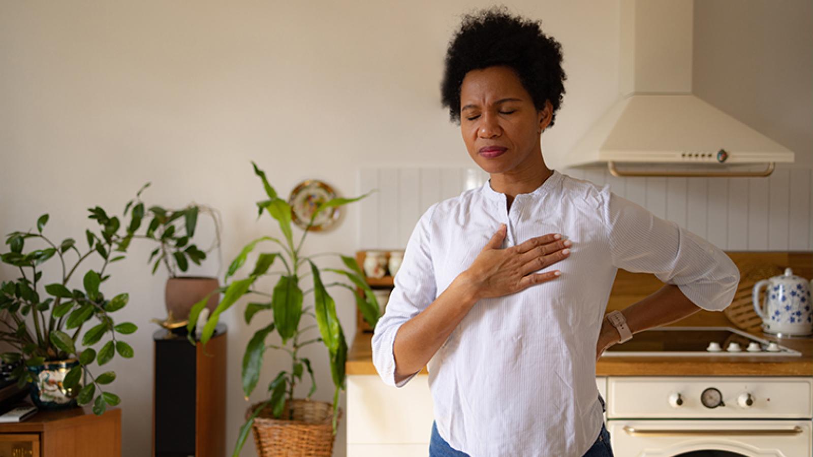 A woman holds her hand to her chest looking pained.