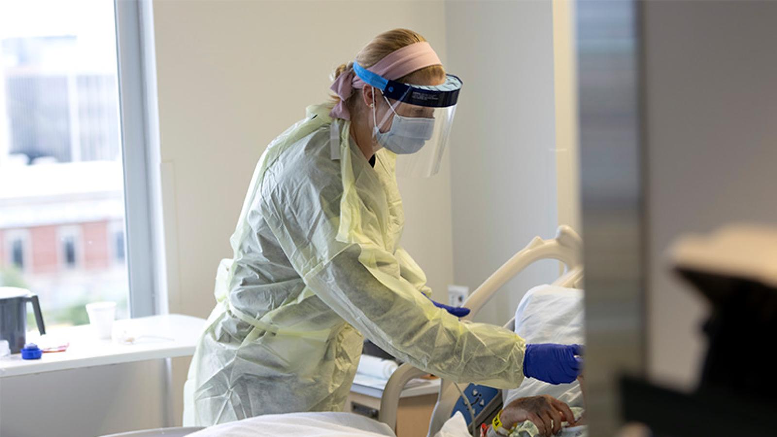 RUSH nurse checking on a patient in a hospital bed during COVID