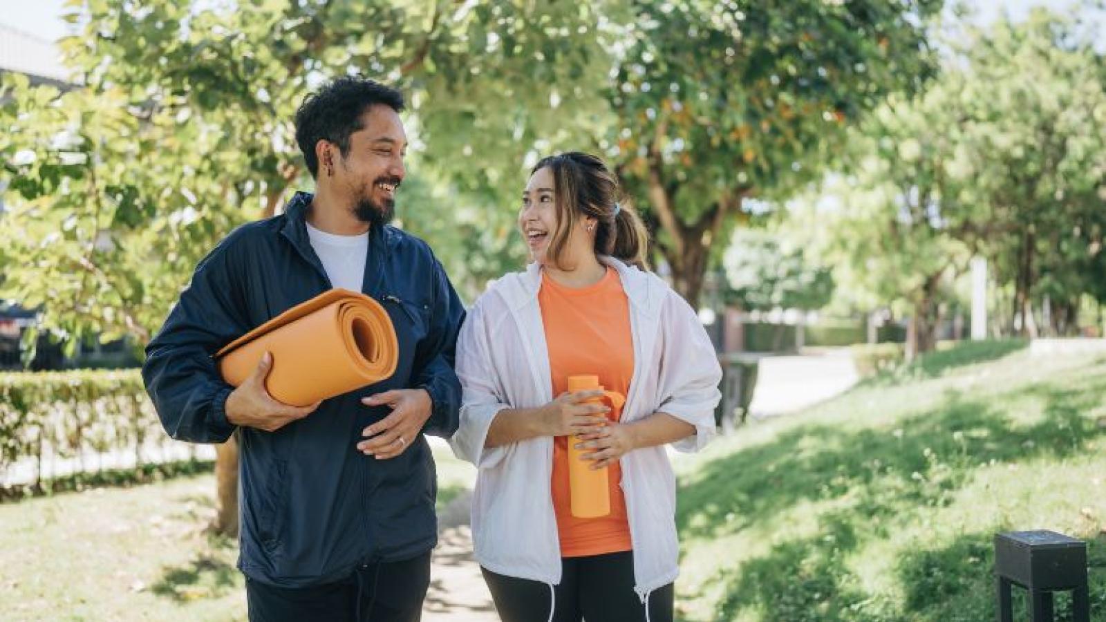 Two people carrying exercise equipment chatting happily in a sunny park.