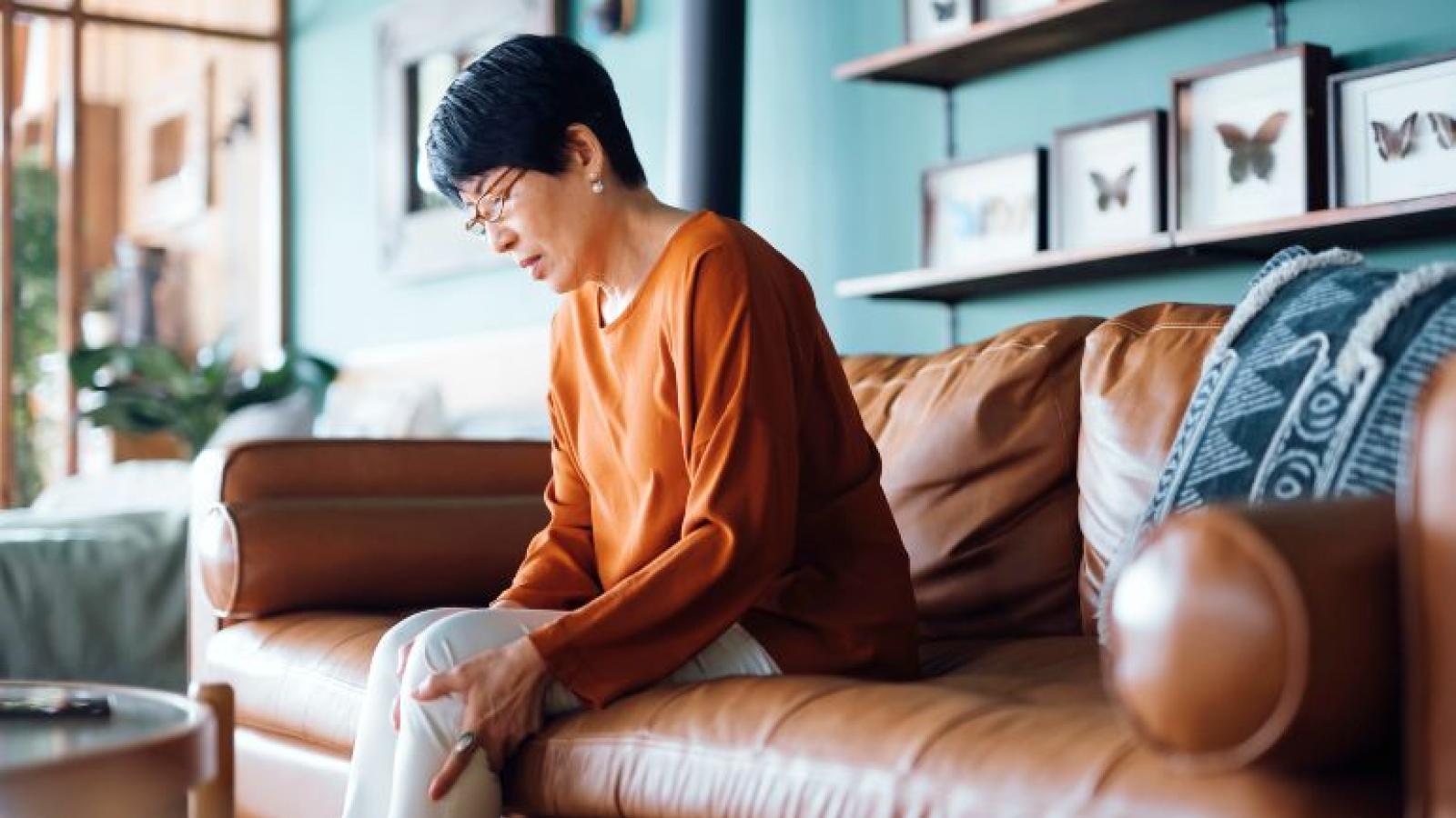 A woman seated on a couch rubbing her knees as though in pain