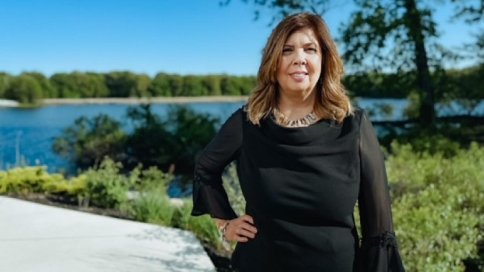 Laura Clancy stands outside on a nature trail in front of a small lake. The sky is bright blue and has no clouds.