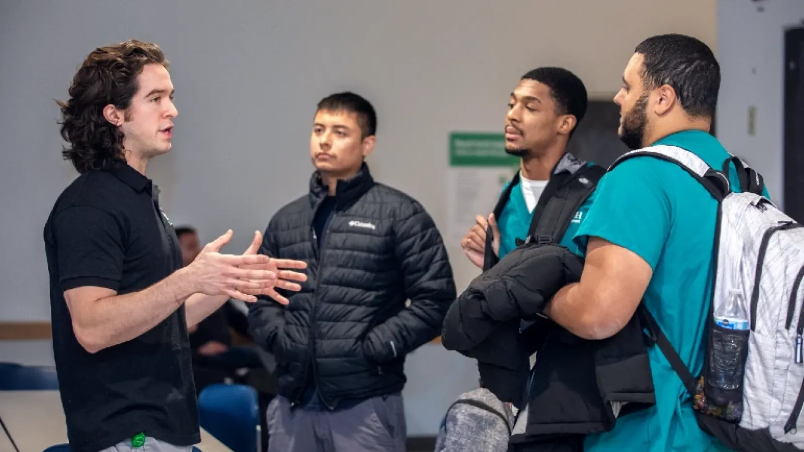 A student gestures with his hands while speaking to three other men wearing scrubs