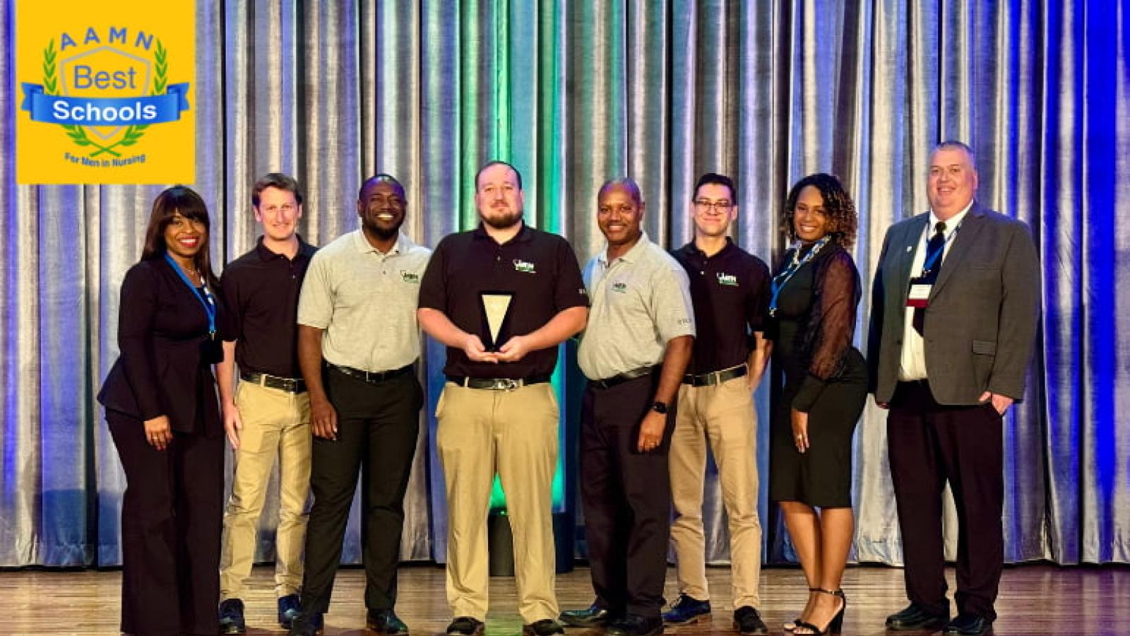A group of students and faculty members standing on a stage holding an award