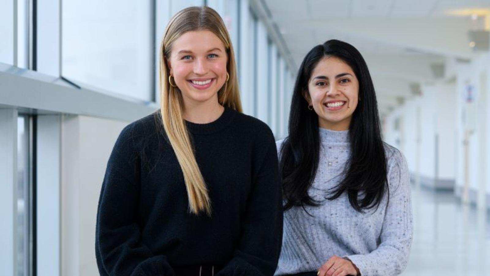 Two women seated in a hallway in front of windows