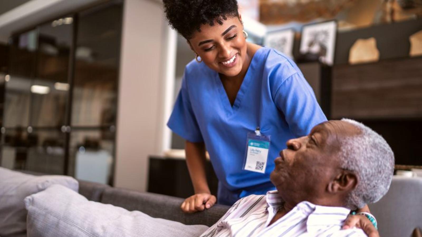 A health care worker leans over to talk with a seated older man