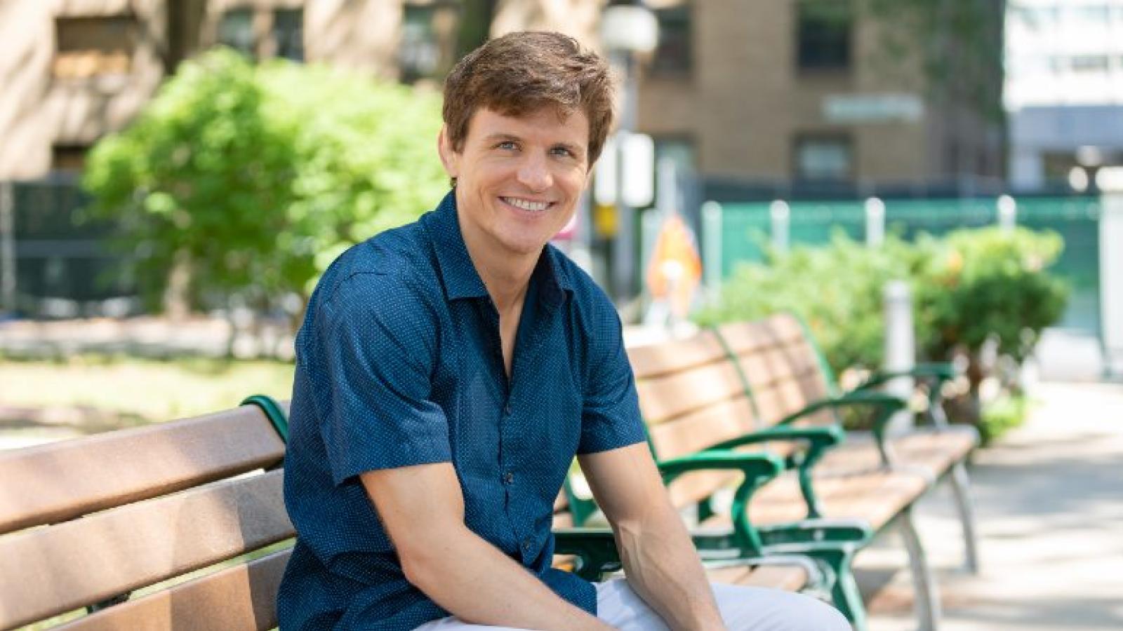 A smiling man seated on an outdoor bench