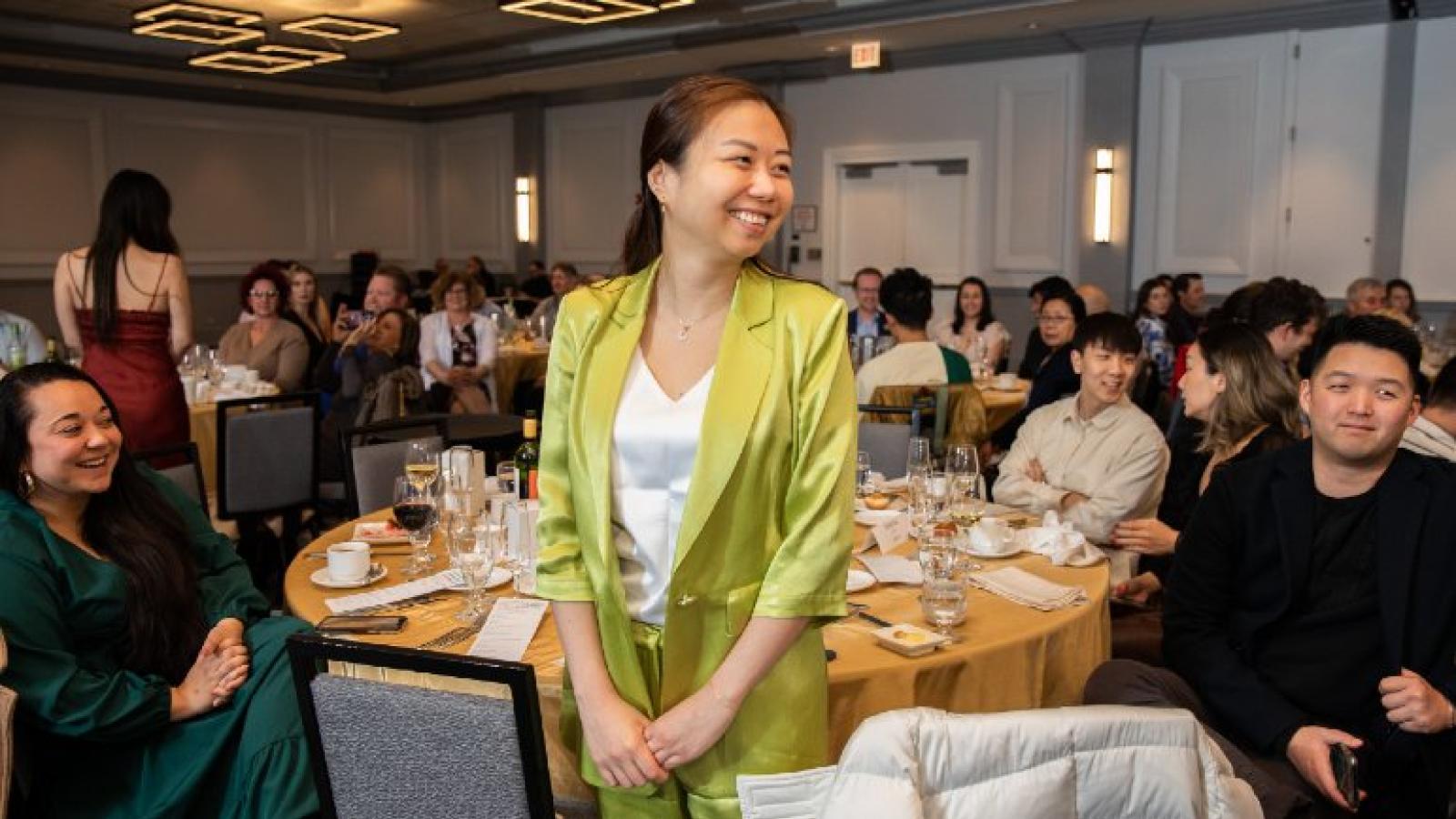 A smiling woman stands in the middle of a crowded banquet room