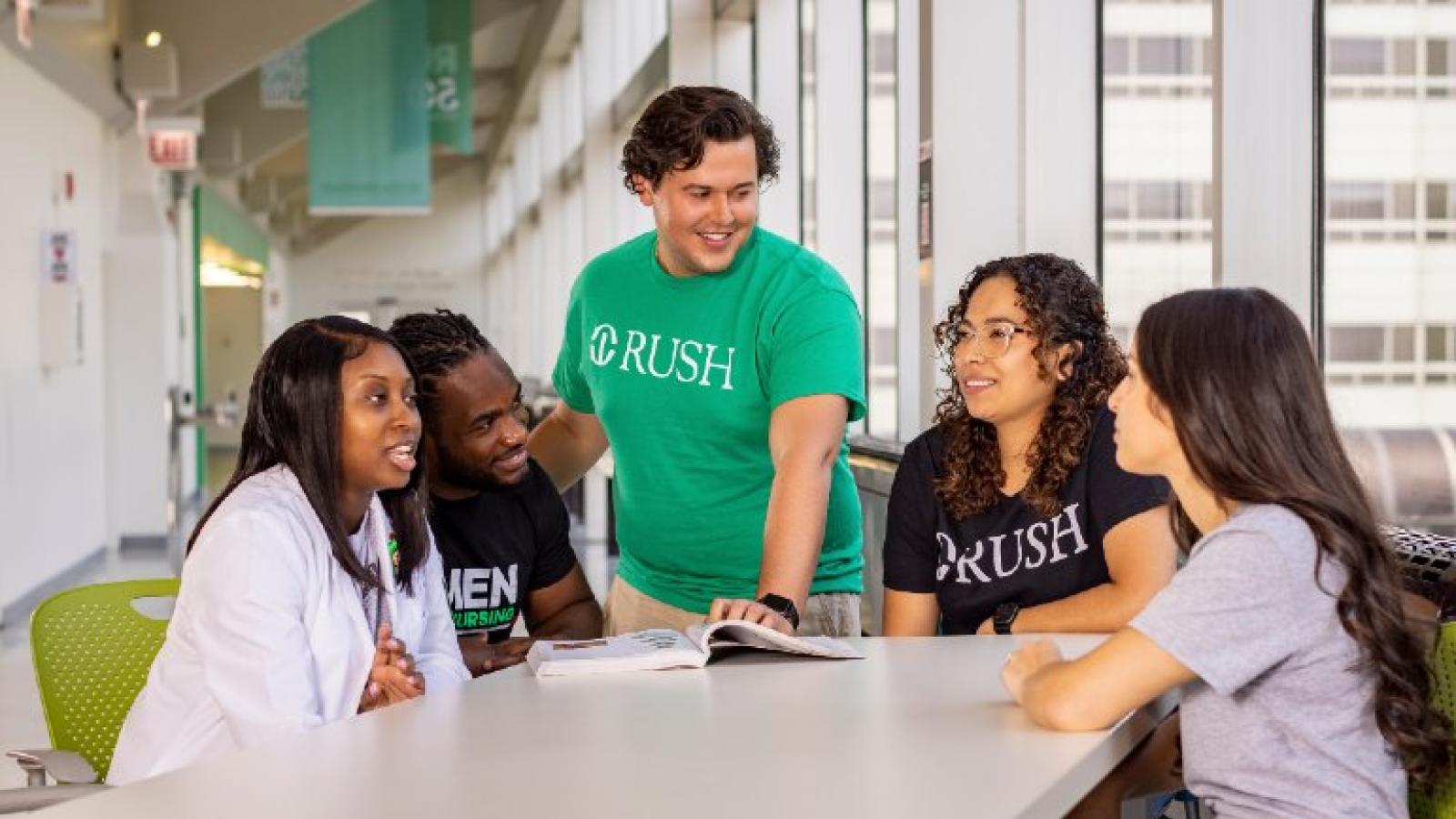 A group of students in conversation with an open textbook on the table in front of them