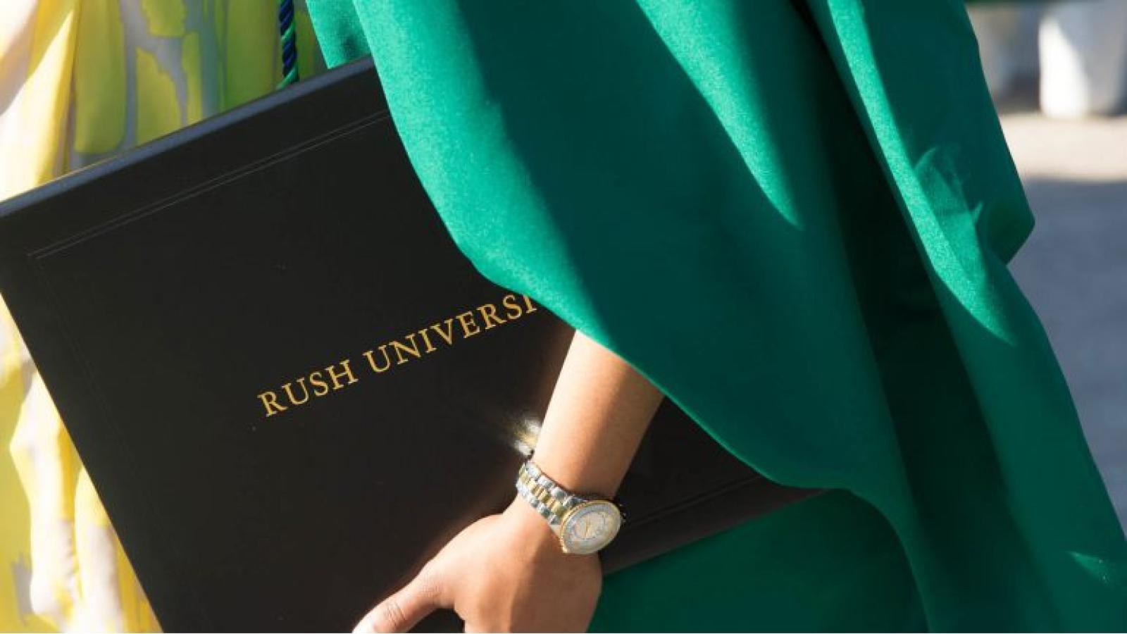 Close-up of a Rush University diploma held by a graduate wearing commencement robes