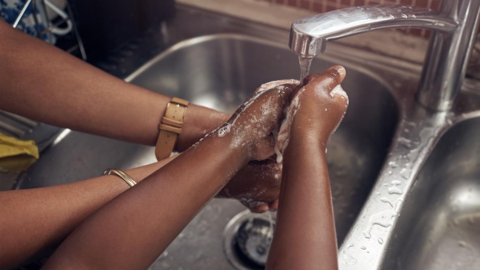 Two people wash their hands in a sink.