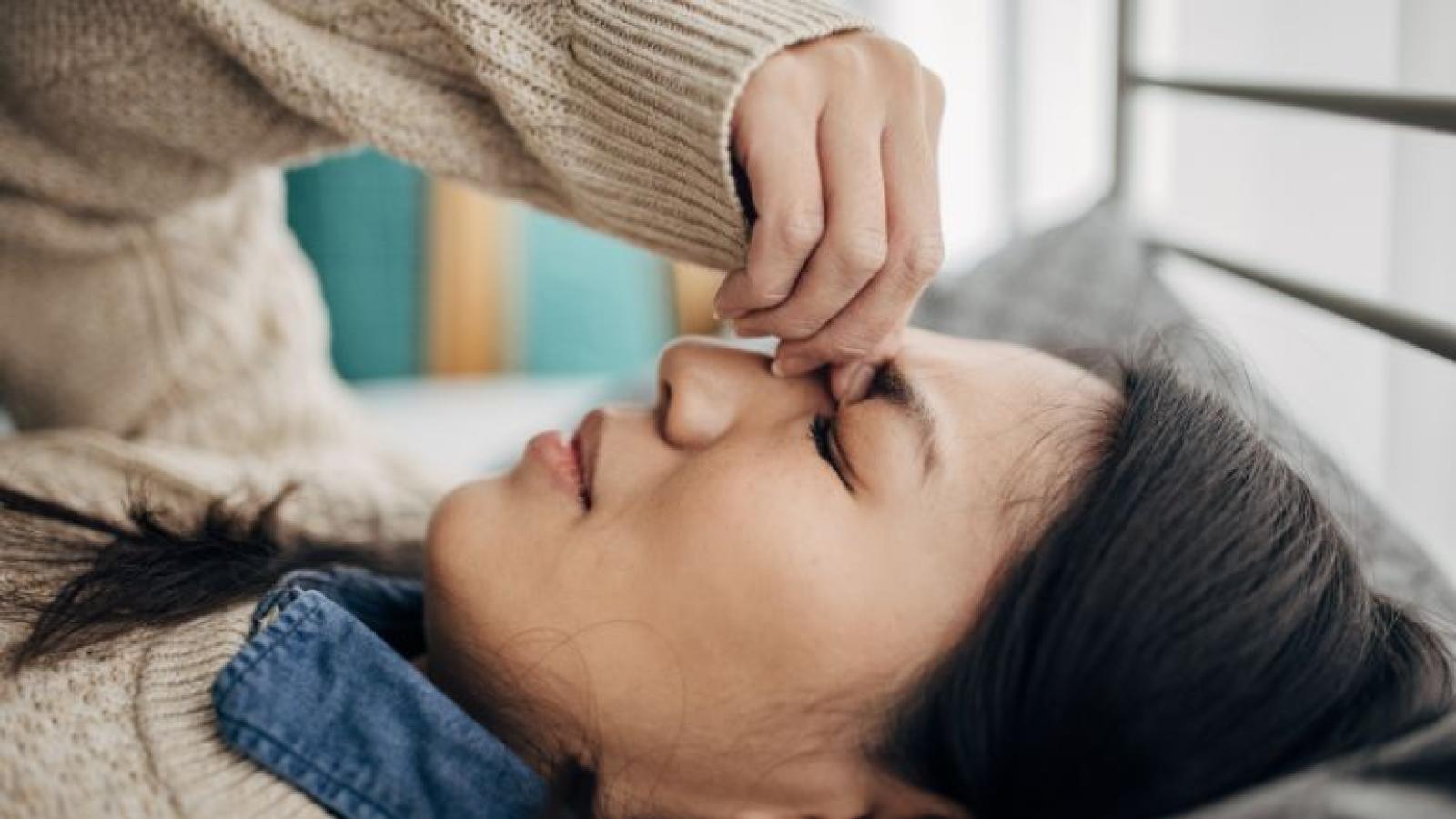Person lying down with eyes closed, gently pressing their forehead with their hand.