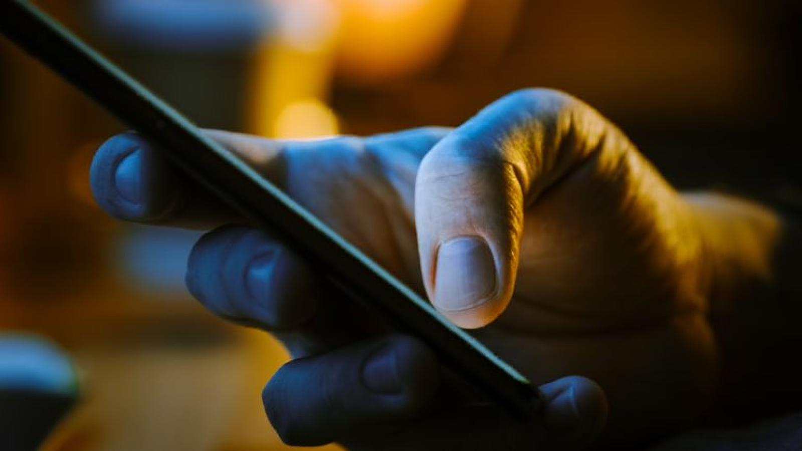 Close-up of a hand holding a smartphone, illuminated in dim light.