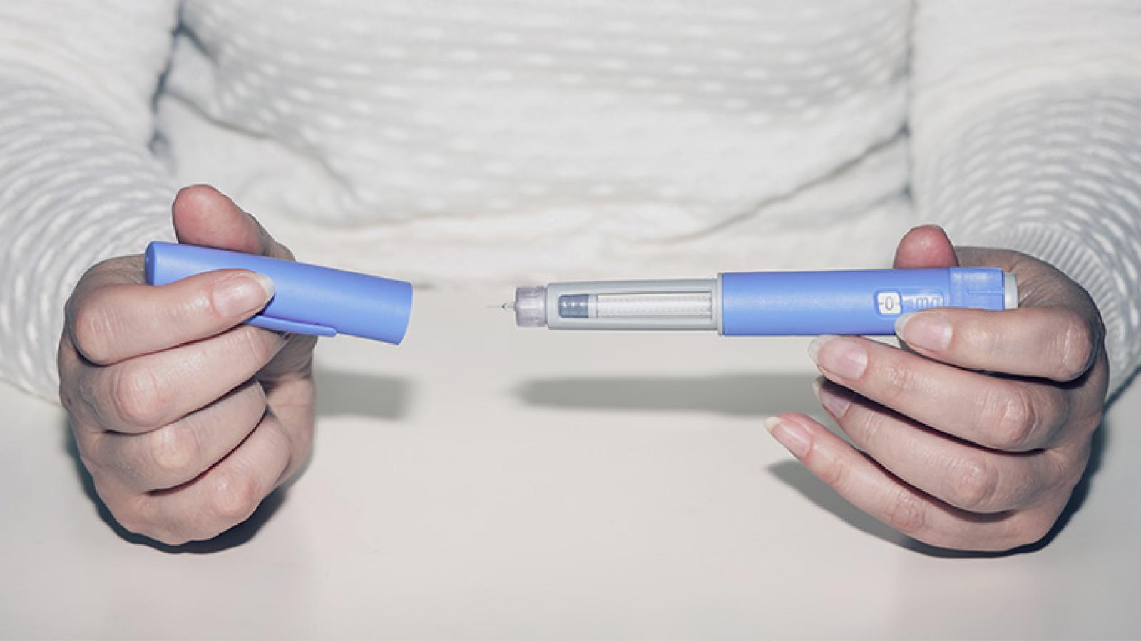 a person in a white knit sweater holding a generic injectable weight loss drug in their hand