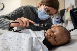 A nurse checks the ear of an infant.