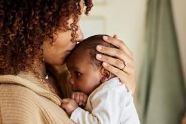 A mother holding a baby on her chest and kissing the baby's head.
