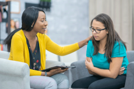 Black female care provider with hand on shoulder of female patient of color