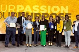 A group of students and faculty pose on a stage holding award certificates