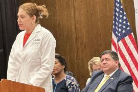 Dr. Laura Laursen speaks. Gov. J.B. Pritzker in the background