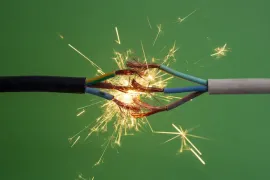 Electrical sparks fly away from frayed wires on a green background.
